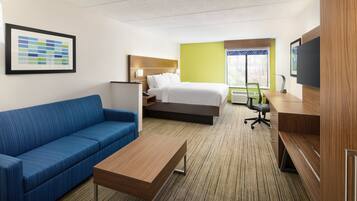 A hotel room with a bed, a blue sofa, a wooden desk, and a television.