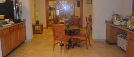 A kitchen with wooden cabinets, a refrigerator, a dining table with chairs, and a small side table with a vase.