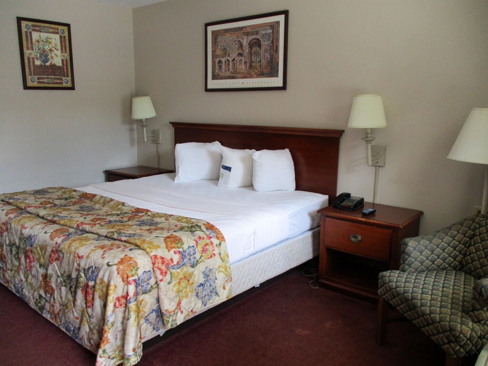 Habitación de hotel con una cama grande, dos mesitas de noche, una silla y dos lámparas de pared.