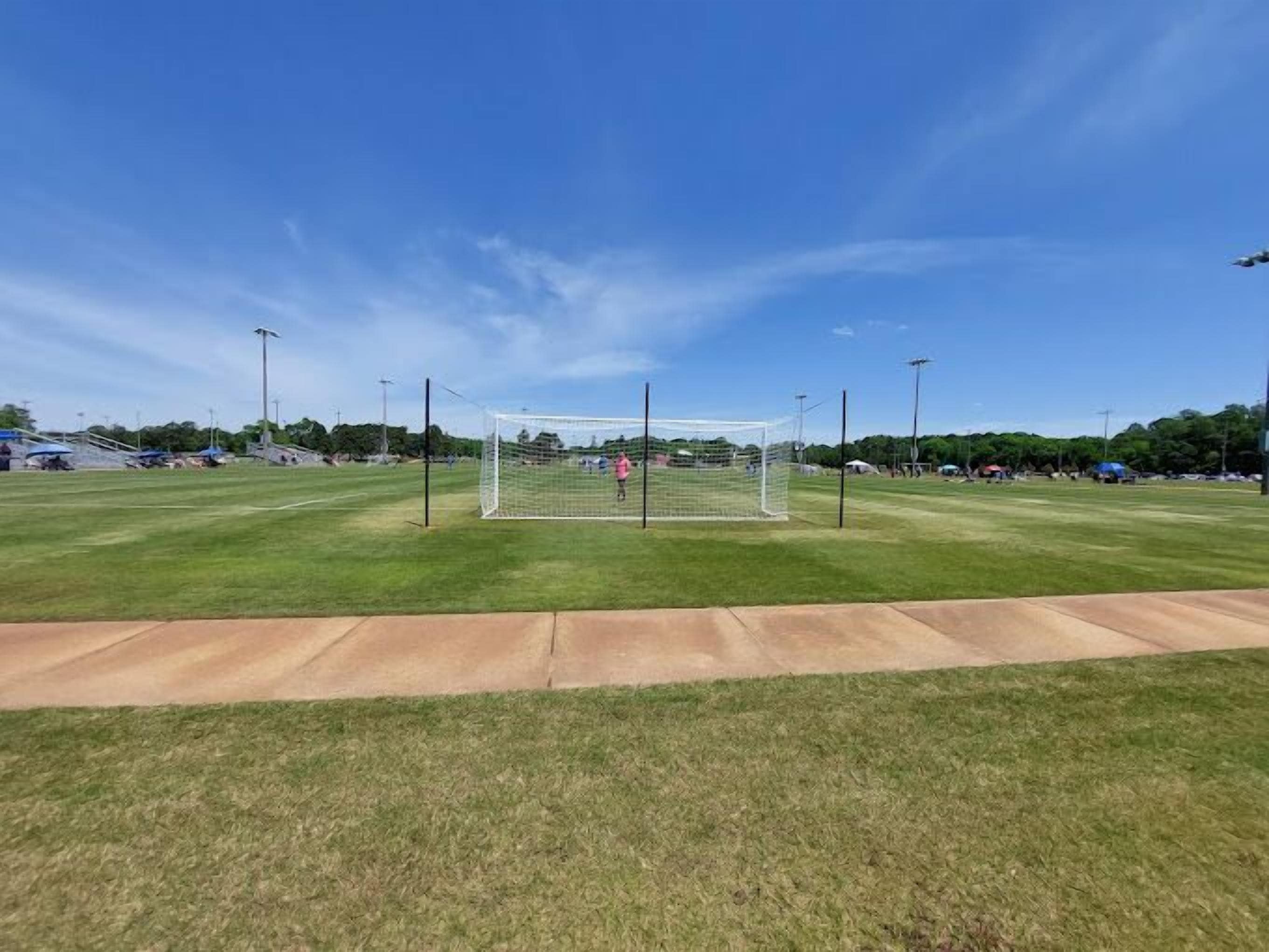 A soccer field with a goalpost, surrounded by a clear sky and a well-maintained lawn.
