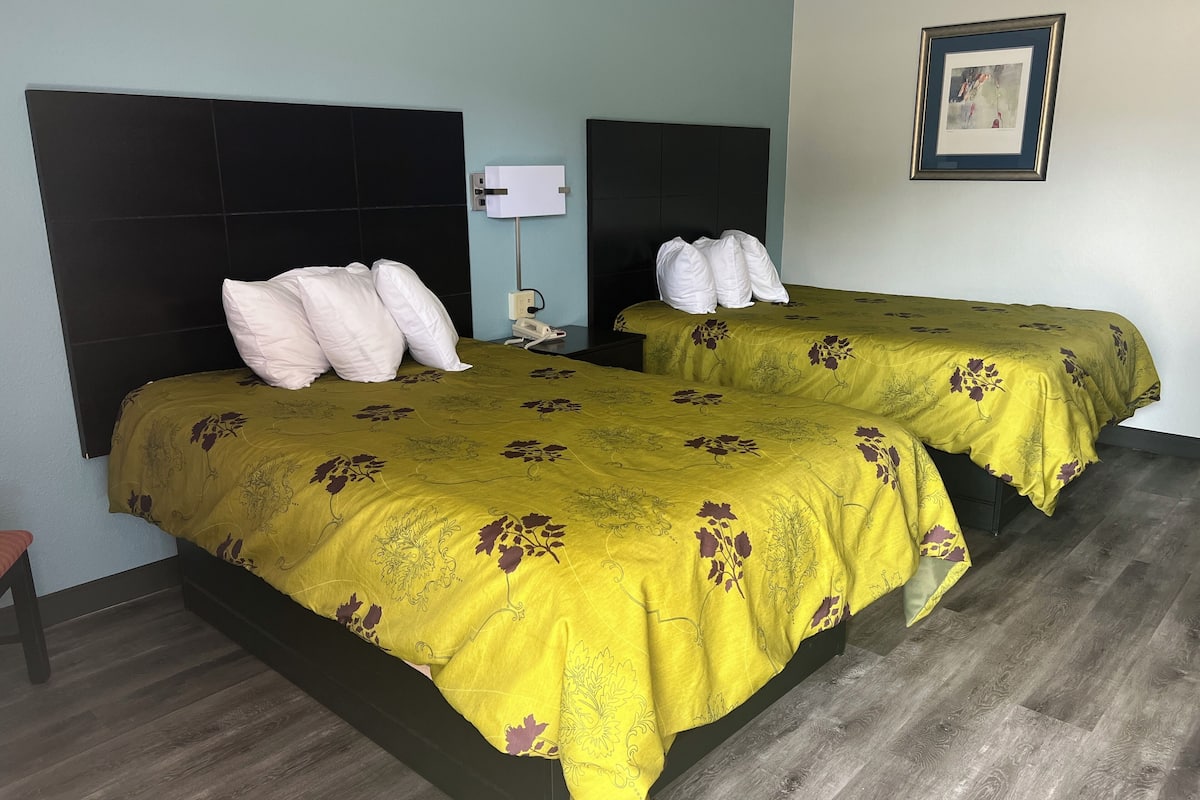 A hotel room with two beds, each with a black headboard and a floral bedspread. There is a nightstand with a lamp and a phone between the beds.