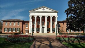 A large, symmetrical building with a central entrance flanked by columns, surrounded by a well-maintained garden with red flowers. - American Inn  - Pontotoc (Pontotoc)