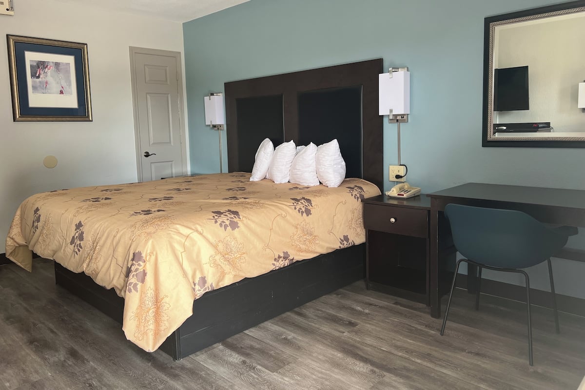 A hotel room with a bed, a desk, a chair, a telephone, and a mirror.