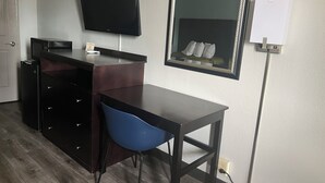 A hotel room with a desk, a chair, a flat-screen TV, a mirror, and a small refrigerator. - American Inn  - Pontotoc (Pontotoc)