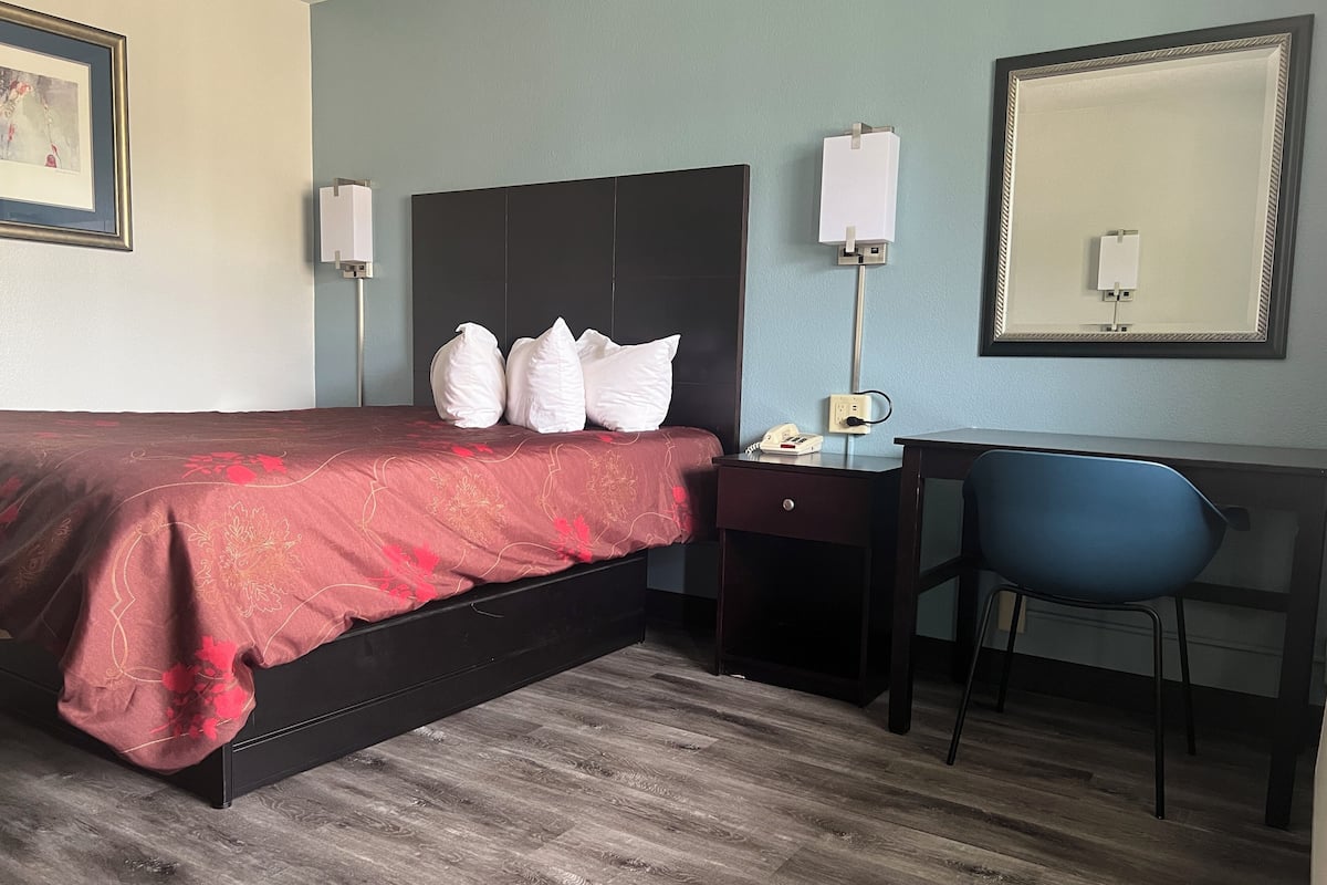 A hotel room with a bed, a desk, a chair, and a large mirror.