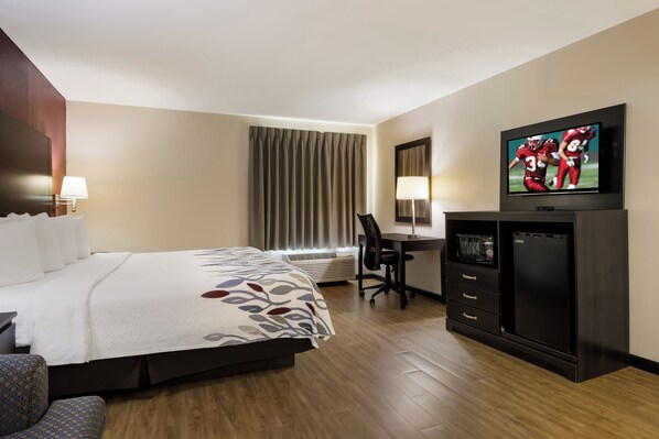 A hotel room with a bed, a desk, a television, and an air conditioning unit.