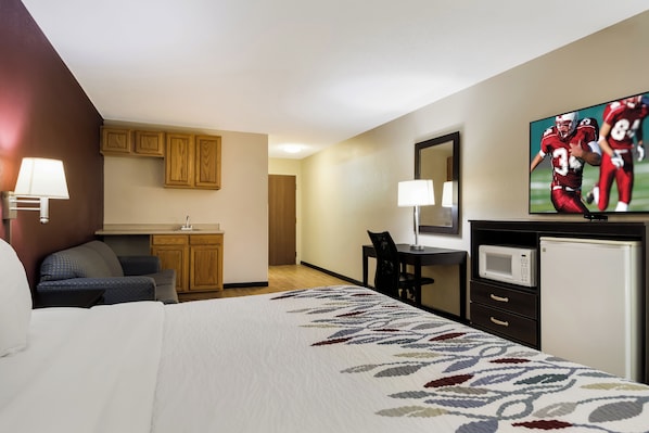 A hotel room with a bed, a desk, a microwave, a TV, and a seating area with a chair and a sofa.