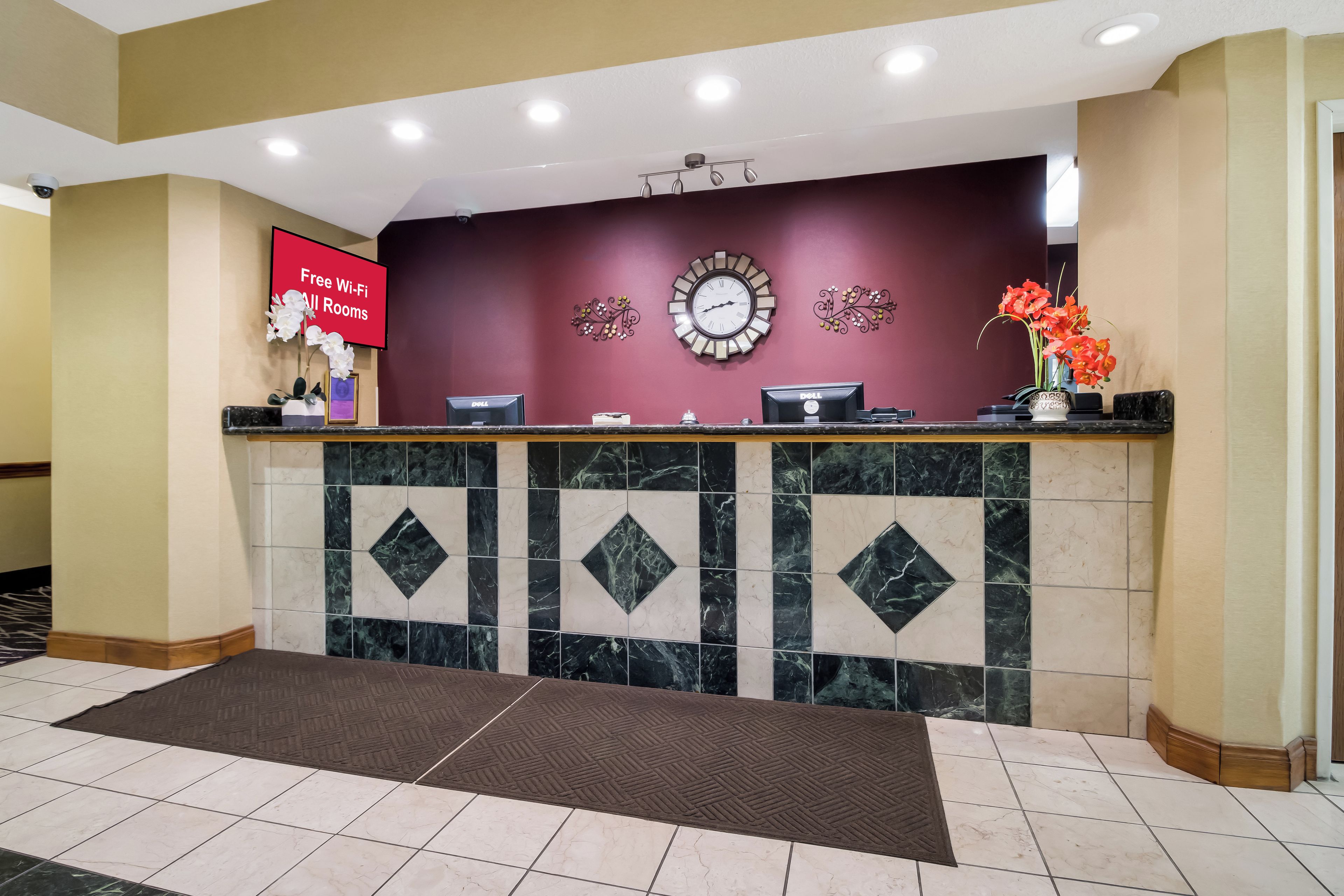 A hotel reception desk with a digital screen, a clock, and a vase of flowers.