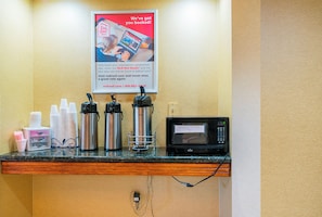 Un espace d’accueil d’hôtel avec une affiche publicitaire pour Red Roof Inn, un coin café avec des gobelets jetables, un four à micro-ondes et une bouilloire.