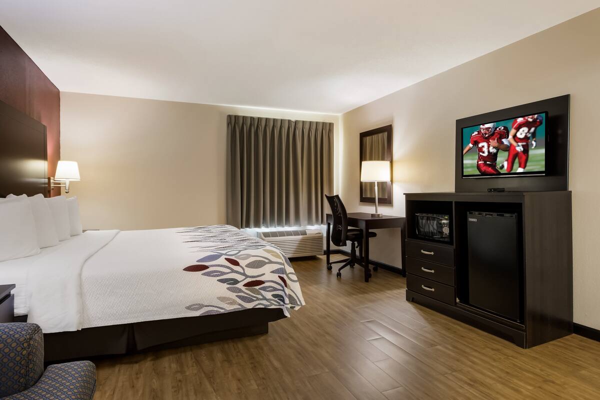Een hotelkamer met een bed, bureau, televisie en een minibars.