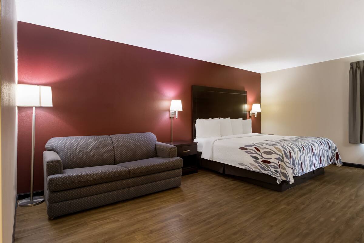 Una habitación de hotel con sofá, cama con colcha estampada, dos lámparas de noche y suelo de madera.