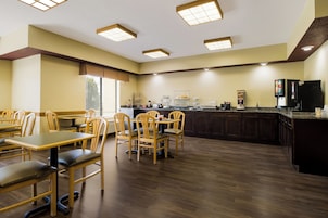 A restaurant with wooden chairs and tables, a kitchen area, and a coffee machine.