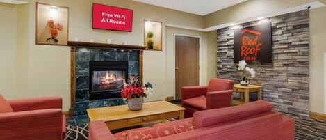 Un vestíbulo de hotel con chimenea, muebles tapizados en rojo, un letrero de Red Roof Inn y un letrero que dice 'Wi-Fi gratuito en todas las habitaciones'.