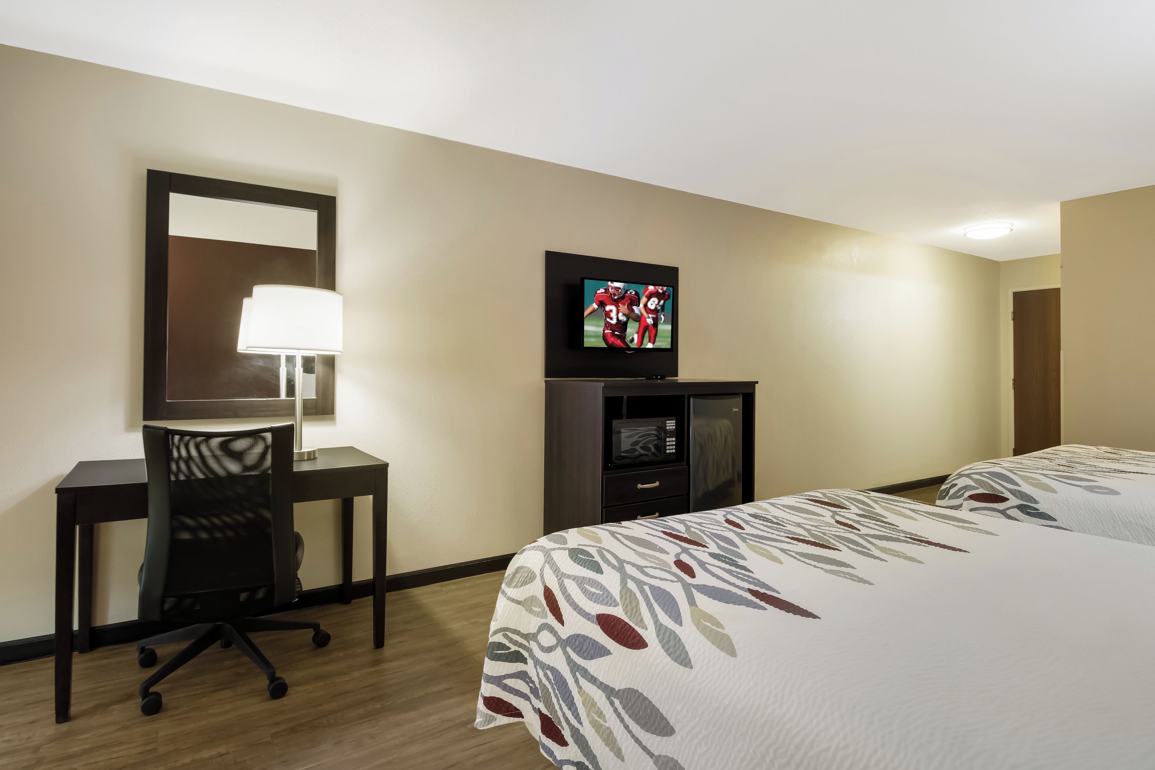 Ein Hotelzimmer mit einem Bett, einem Schreibtisch mit Stuhl, einem Fernseher und einer Lampe.