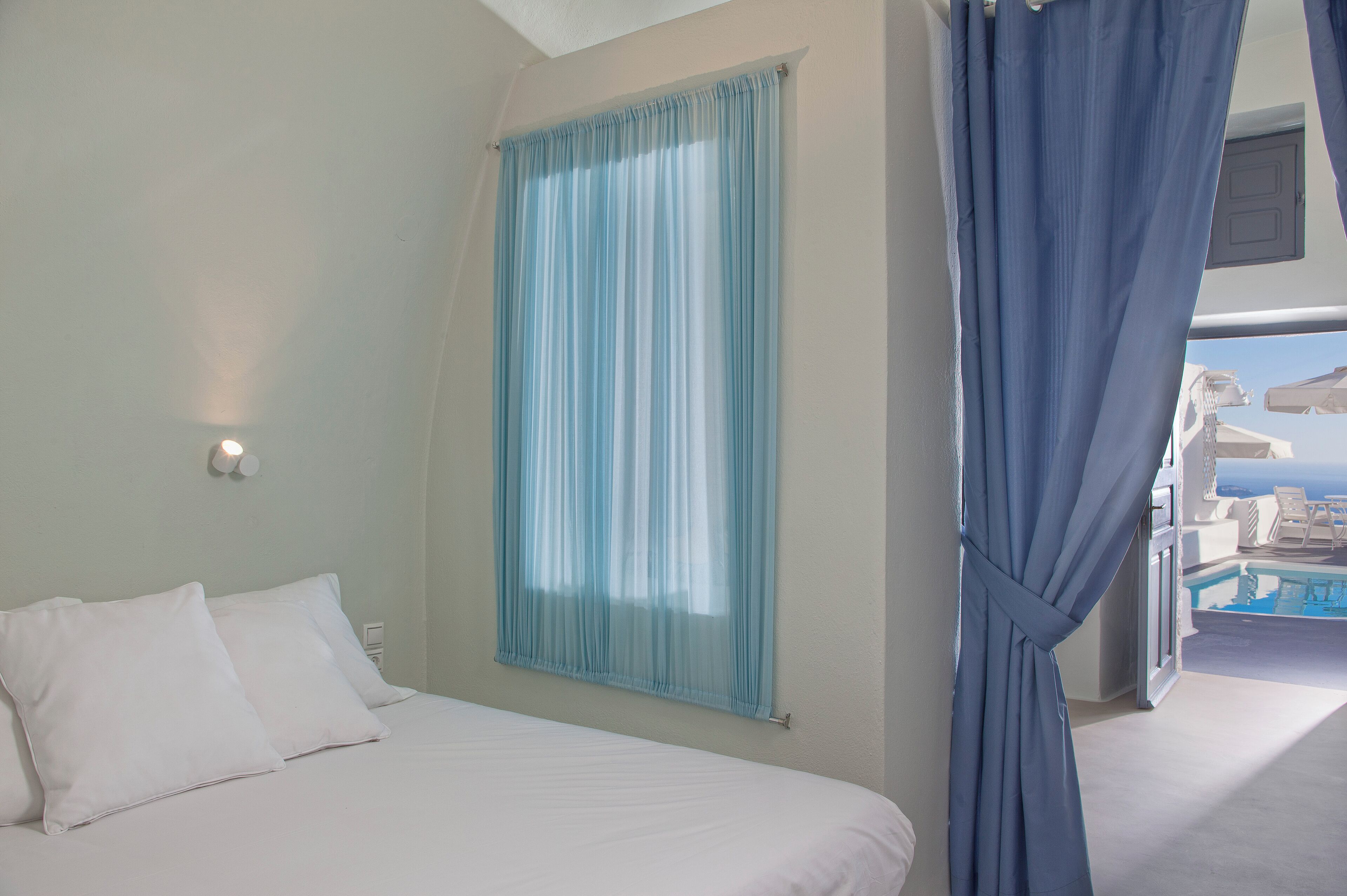 Habitación de hotel con cama, ventana con cortinas y vista a una piscina y un edificio.