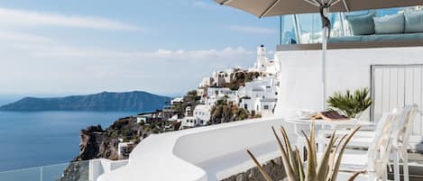 A white outdoor seating area with a view of a coastal town and the sea.