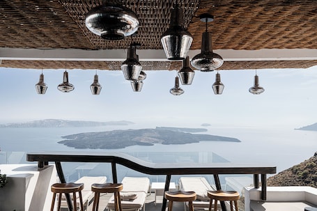 A terrace with a view of the sea, hanging pendant lights, and bar stools.