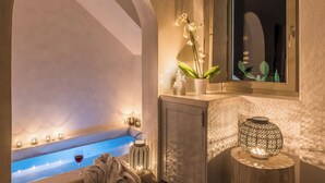 A modern bathroom with a bathtub, a vanity with a mirror, and decorative lighting. - On The Rocks Hotel (Santorini)