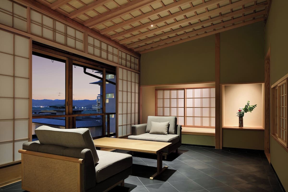 A traditional Japanese-style room with tatami flooring, a low table, and two cushioned seating areas.