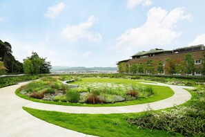 A landscaped garden with a curved pathway, a central lawn, and a building with a green roof in the background.