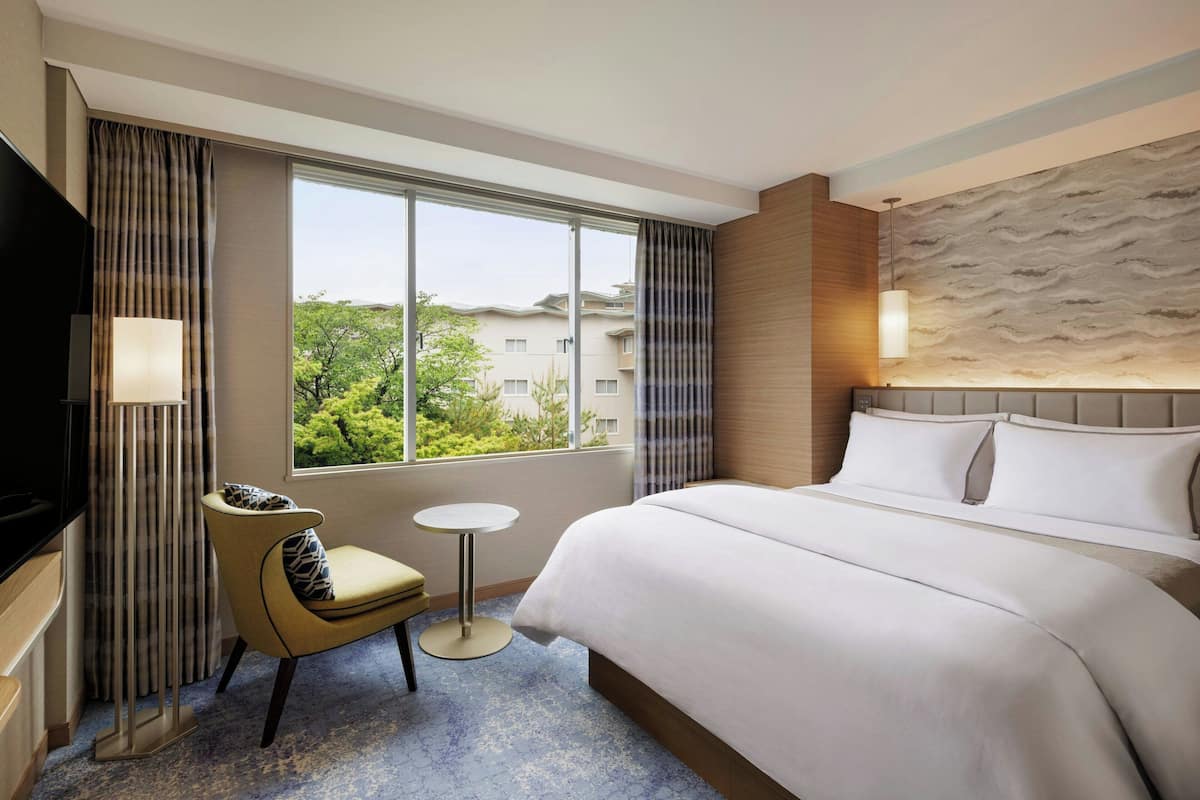 A hotel room with a large bed, a TV, a small table, and a chair.