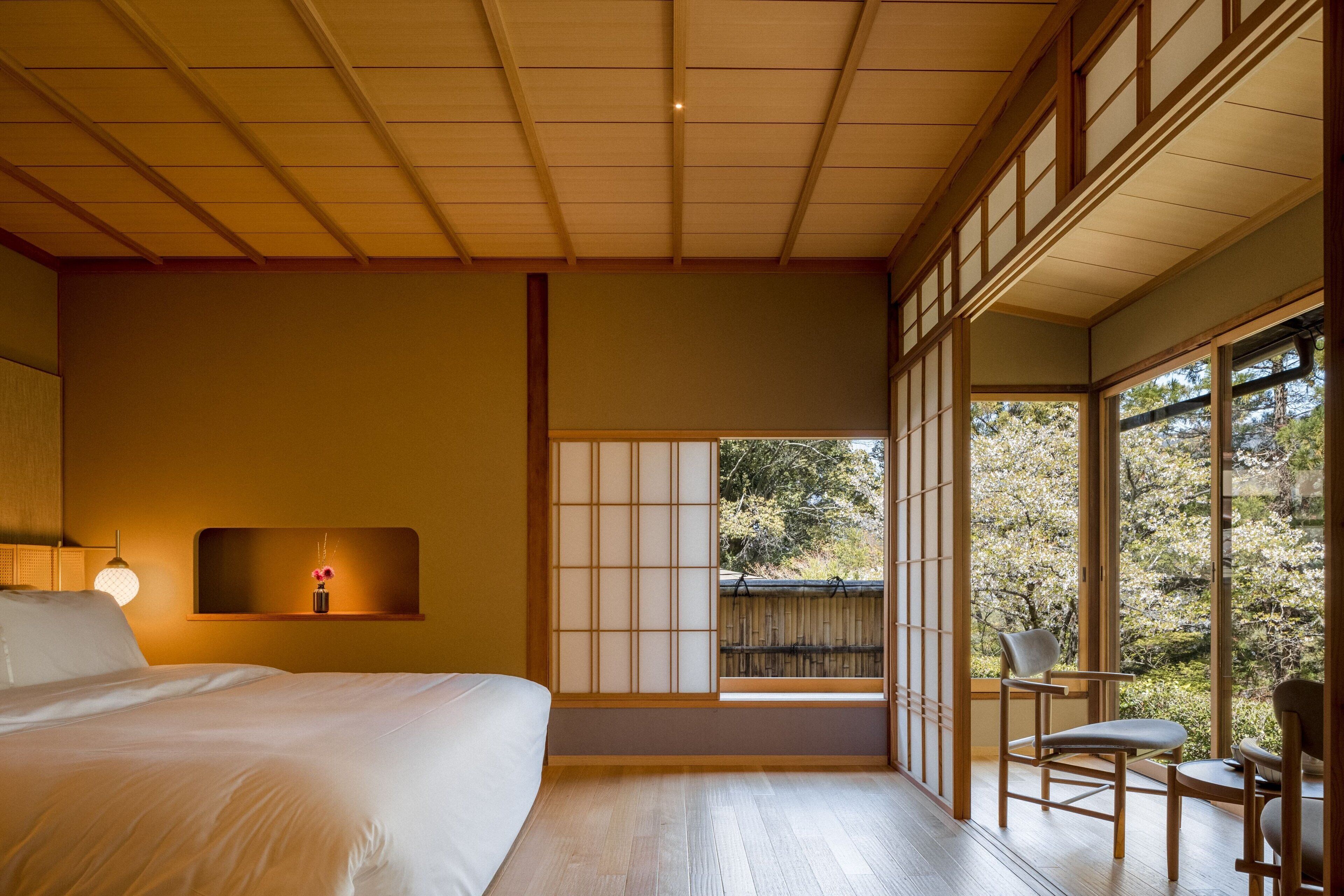 A traditional Japanese-style bedroom with a large bed, sliding shoji doors, and a view of a garden.