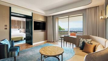 Una habitación de hotel moderna con sofá, una mesita redonda, televisor, cama y balcón con vistas.