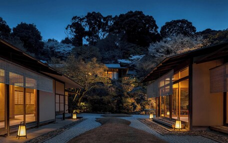 A traditional Japanese-style building with a wooden exterior and large windows, surrounded by a garden with a gravel path and lanterns.