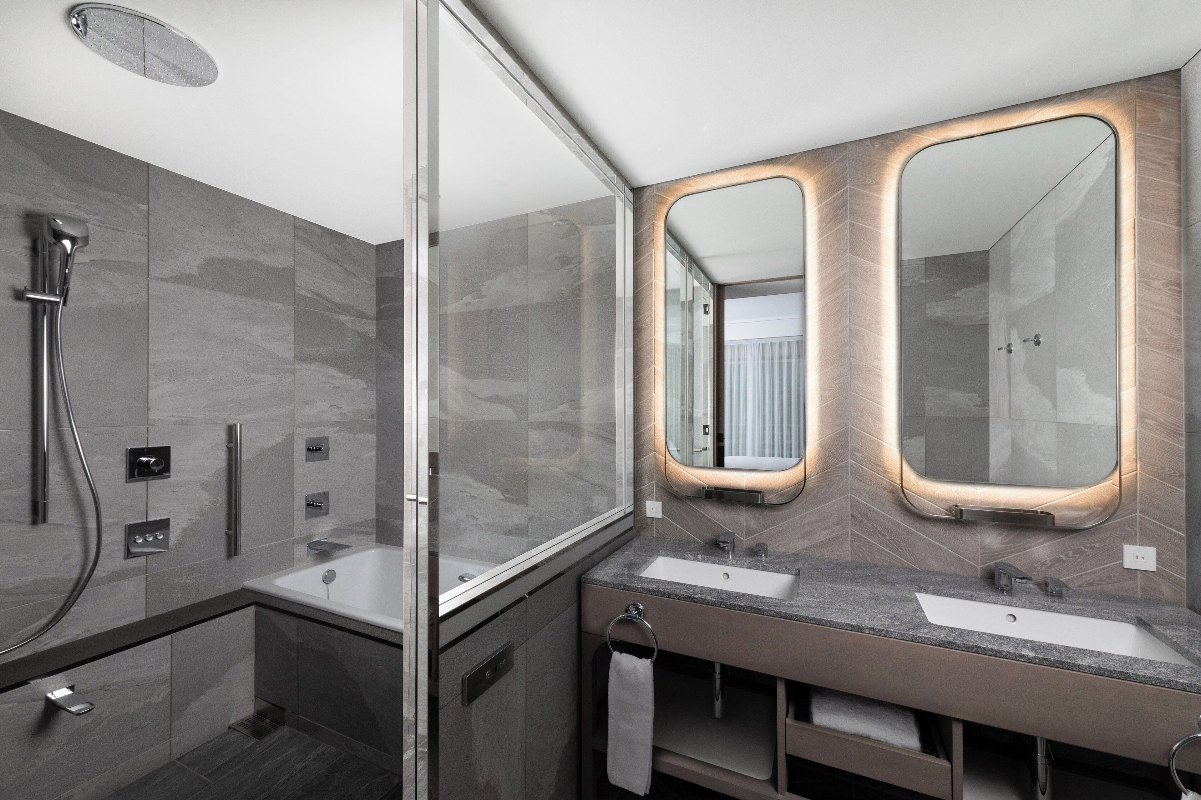 A modern bathroom with a glass-enclosed shower, two sinks, and a large mirror with illuminated frames.