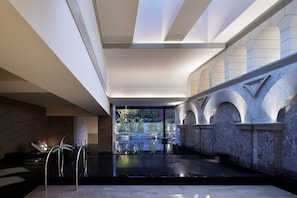 A modern indoor pool area with a clear view of the outdoors, stone walls, and a minimalist design.