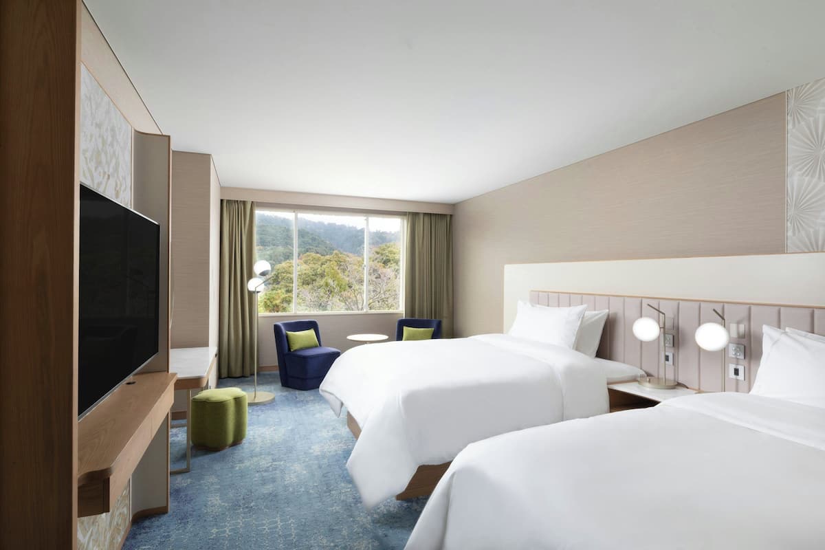 A hotel room with two beds, a TV, a desk, and a view of the outdoors.