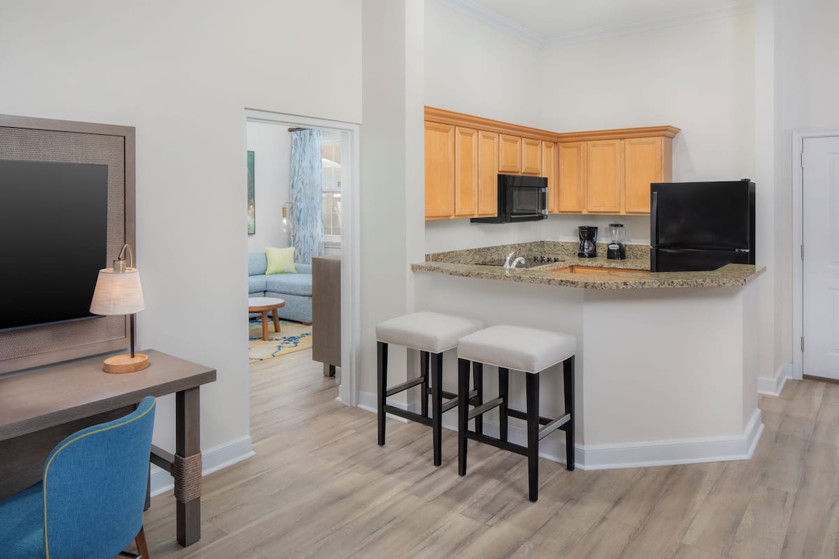 A modern kitchen with wooden cabinets, a black refrigerator, and a granite countertop. There are two bar stools and a small island with a sink.
