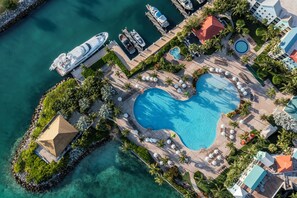 An aerial view of a resort with a large heart-shaped pool, multiple boats docked, and a variety of buildings and amenities. - Harborside Resort & Vacation Rentals at Atlantis (Paradise Island)