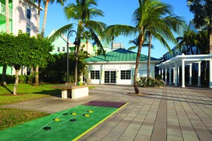 Un patio con una cancha de shuffleboard verde, palmeras y un edificio que dice "JOURNEY ROOM".