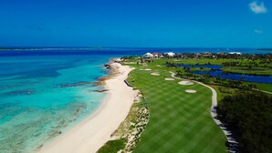 Un campo de golf costero con una playa de arena, aguas azules cristalinas y un césped bien cuidado.