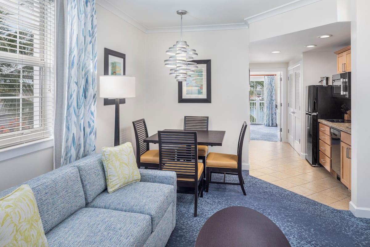 A modern living room with a sofa, dining table, chairs, and a kitchen area with appliances.