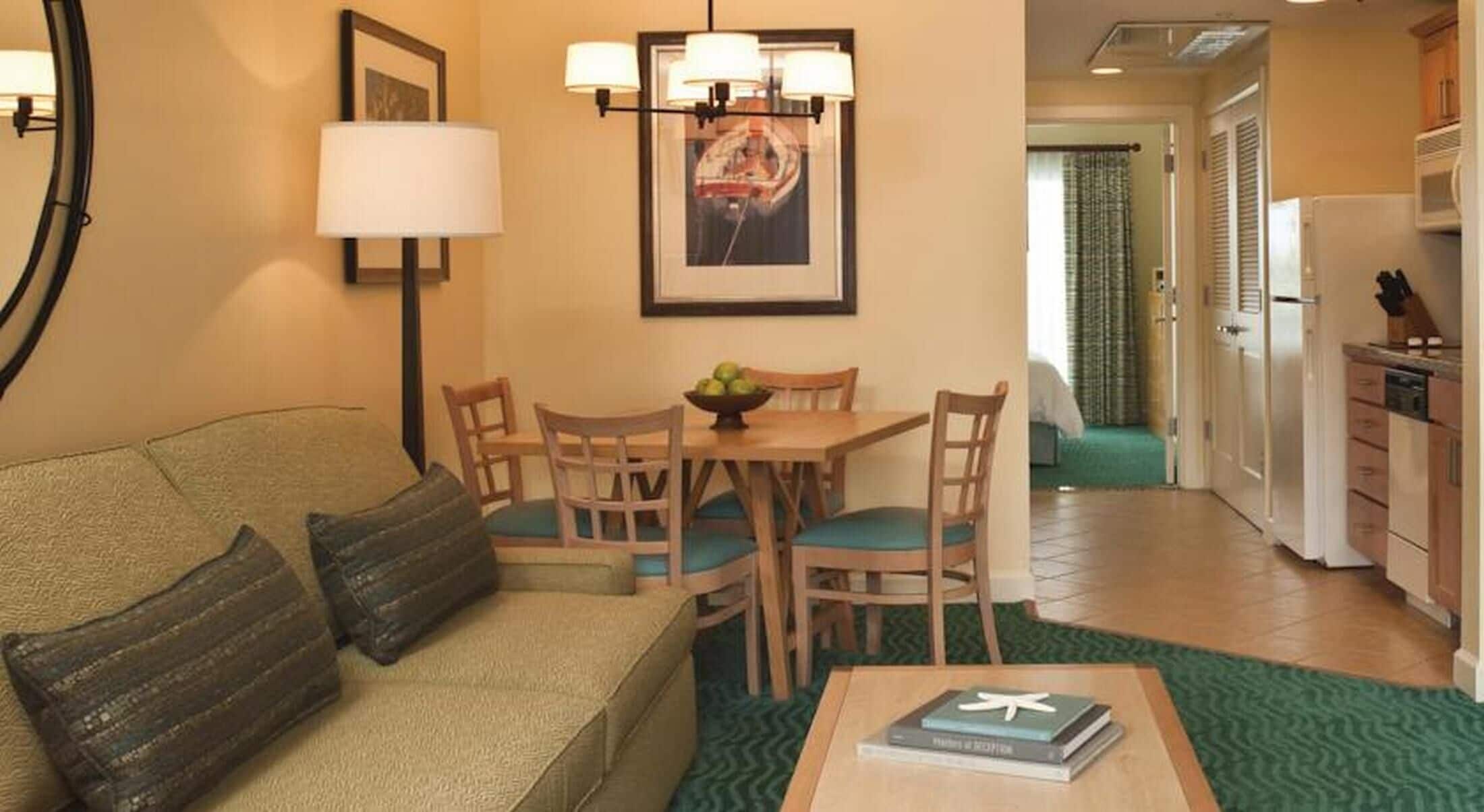 Ein Wohnzimmer mit einer Couch, einem Esstisch mit Stühlen, einer Lampe und einem gerahmten Bild an der Wand.