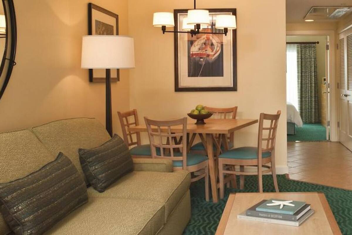 A living room with a sofa, a dining table with chairs, a lamp, and a framed picture on the wall.