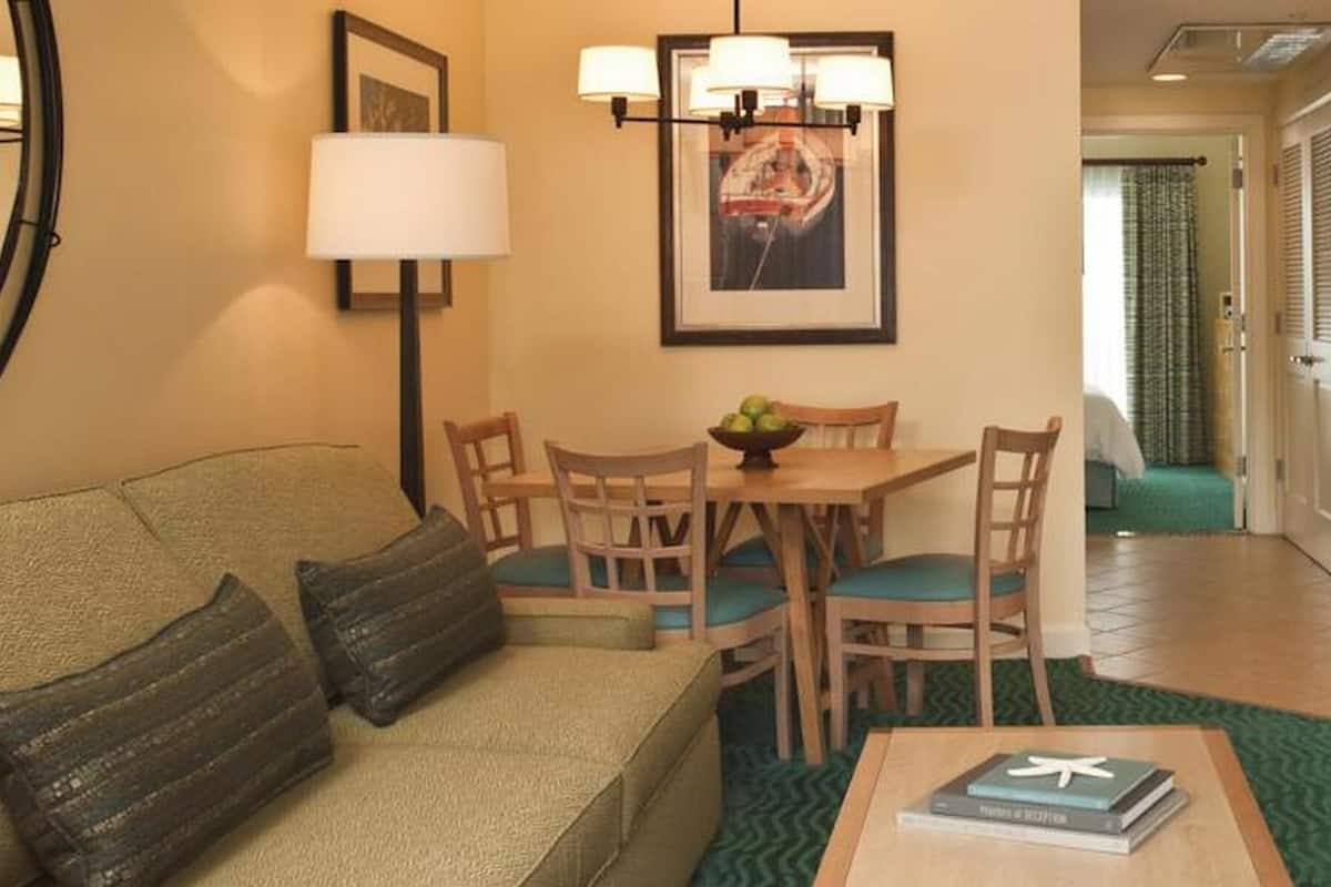 Ein Wohnzimmer mit einer Couch, einem Esstisch mit Stühlen, einer Lampe und einem gerahmten Bild an der Wand.