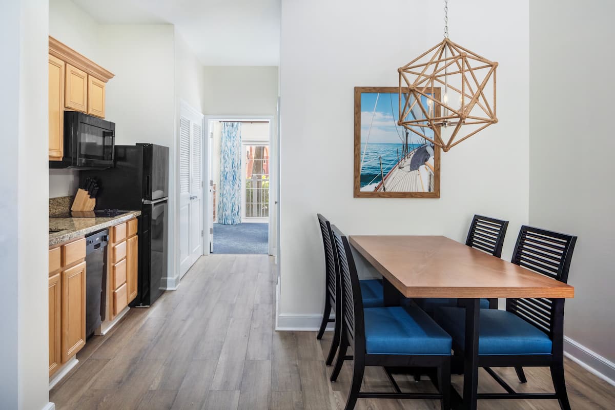 A modern kitchen with wooden cabinets, a black refrigerator, and a dining area with a wooden table and blue chairs.