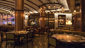 Interior de restaurante con techos altos, paredes de ladrillo visto y varias lámparas colgantes. Las mesas están dispuestas con platos, vasos y cubiertos.