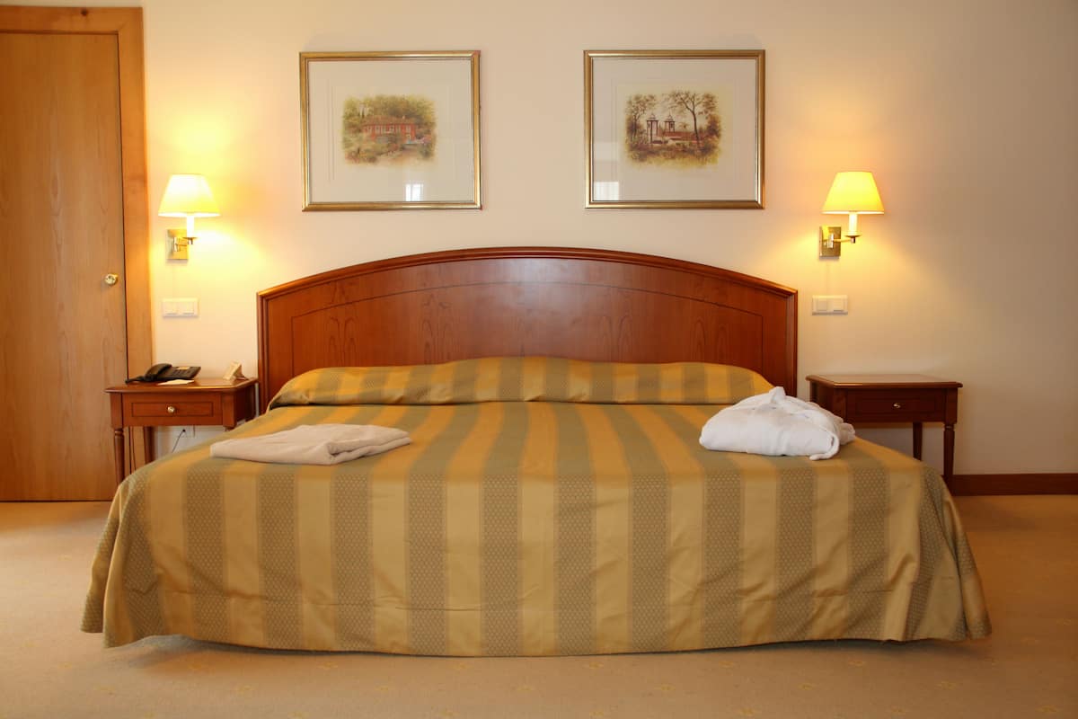 A hotel room with a large bed, two bedside lamps, and two framed pictures on the wall.