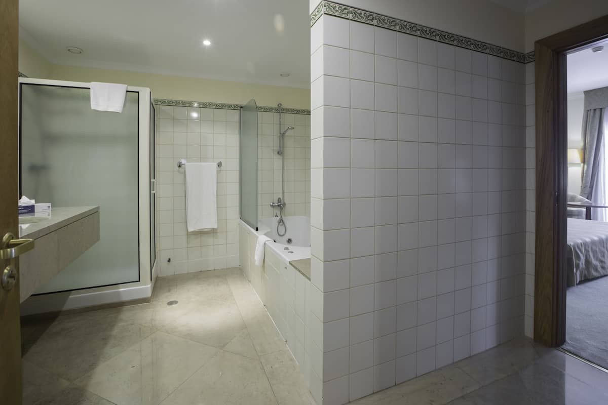 A modern bathroom with a glass-enclosed shower, a bathtub, and a vanity with a towel hanging on the door.