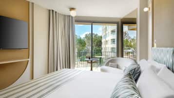 Habitación de hotel con una cama grande, un televisor de pantalla plana, un balcón con mesa y sillas, y vista a la ciudad.