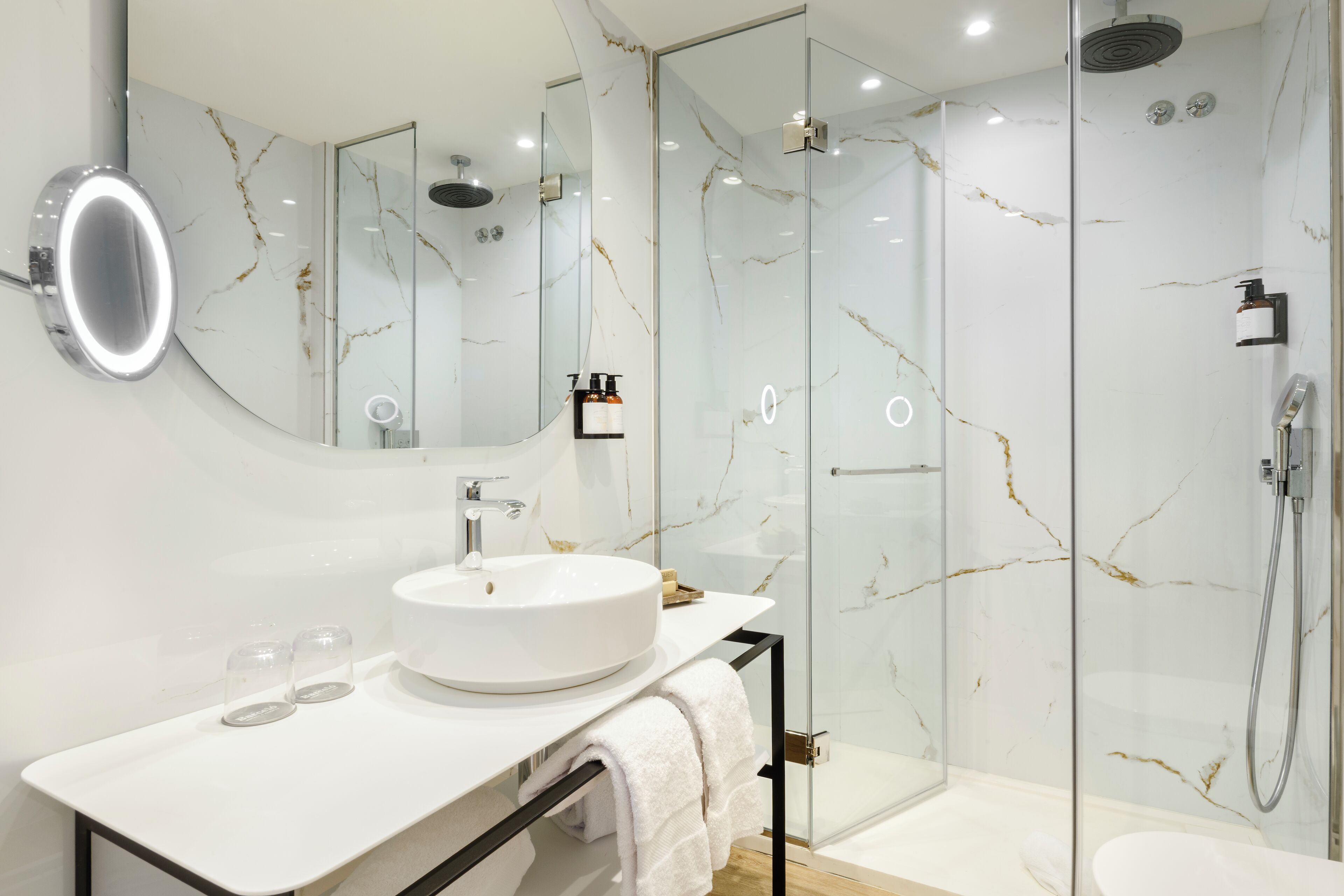 A modern bathroom with a white marble sink, a glass-enclosed shower, and a large mirror.