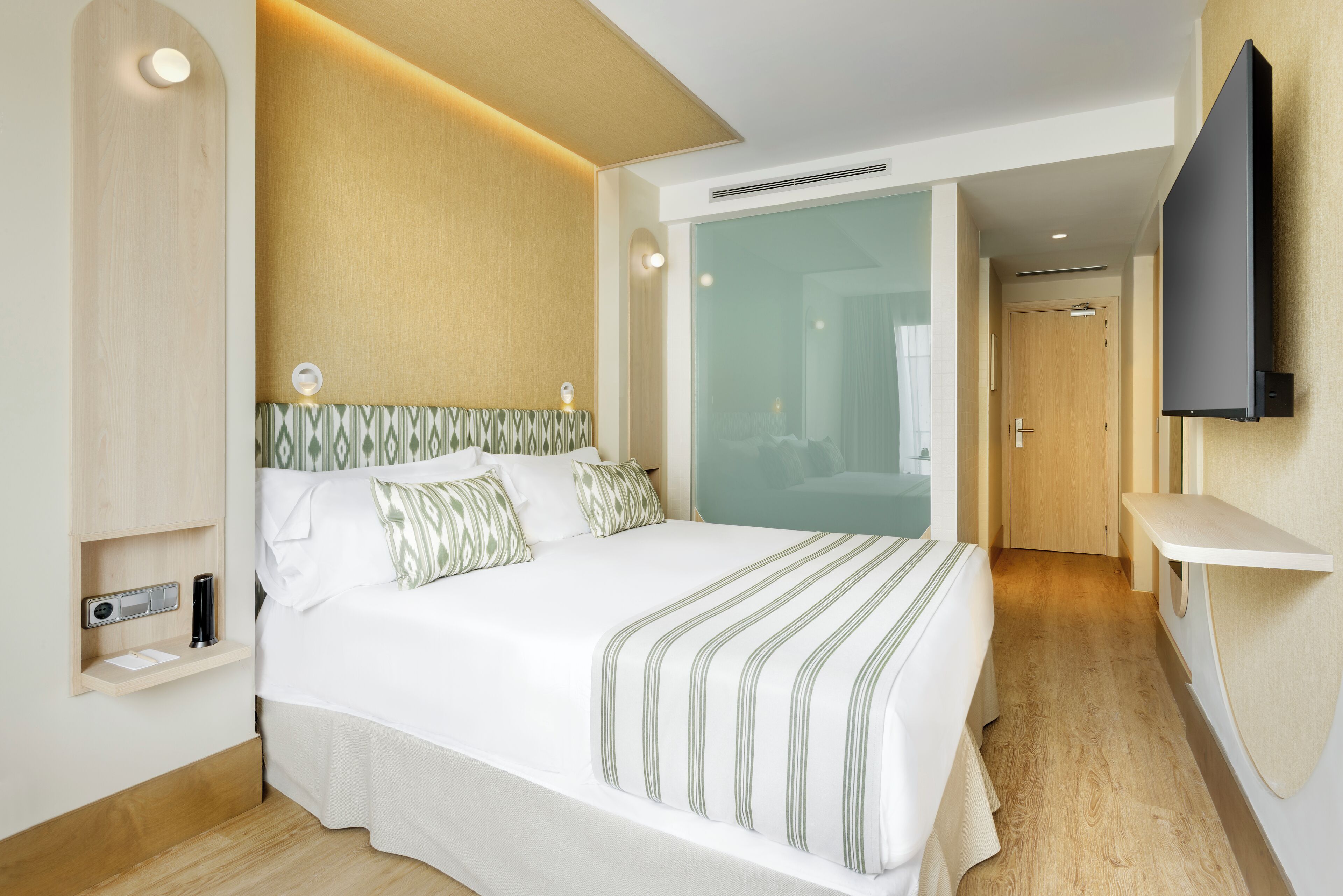 Ein modernes Hotelzimmer mit einem großen Bett, einem Nachttisch, einem an der Wand befestigten Flachbildfernseher und Holzboden.