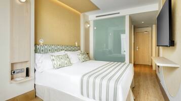 A modern hotel room with a large bed, a bedside table, a flat-screen TV mounted on the wall, and a wooden floor.