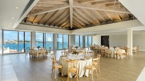 A spacious dining area with round tables set for a meal, large windows offering a view of the sea, and a high wooden ceiling. - Barceló Illetas Albatros - Adults Only (Calvia)