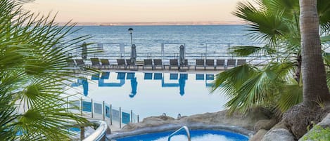 An infinity pool with a view of the ocean, surrounded by palm trees and lounge chairs.