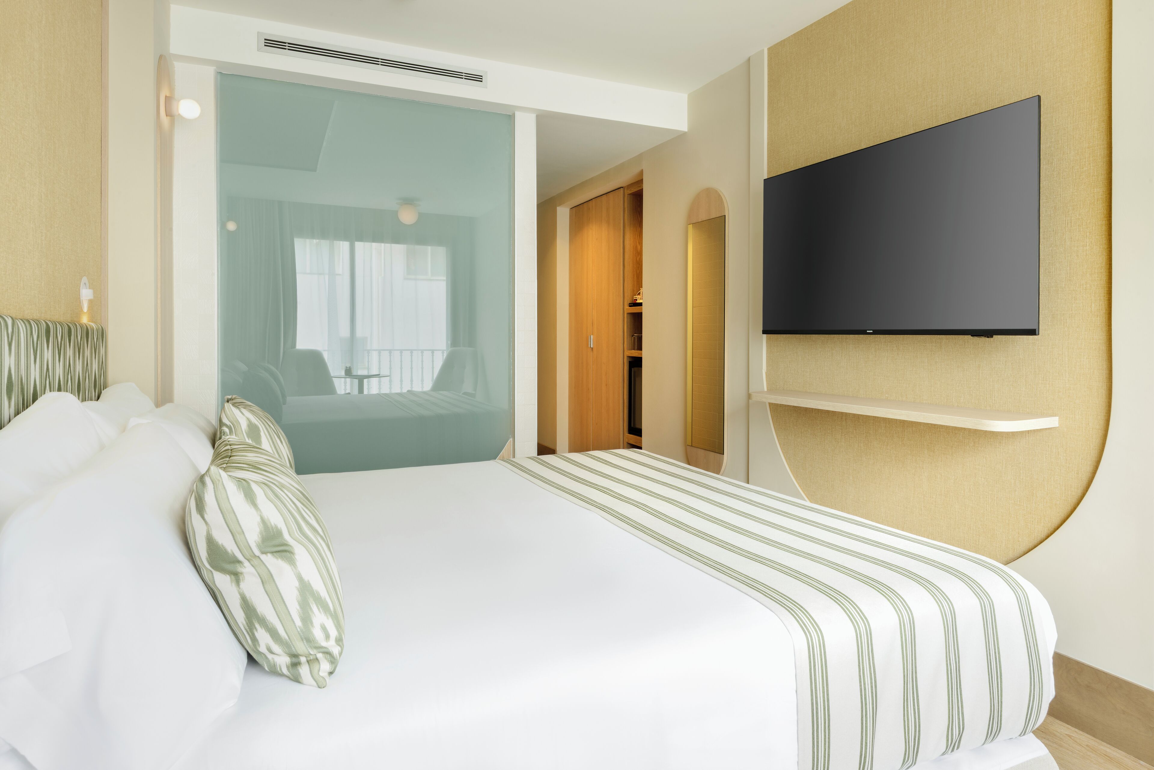 Une chambre d’hôtel comprenant un lit, un téléviseur fixé au mur, un dressing et une porte-fenêtre donnant sur un balcon.